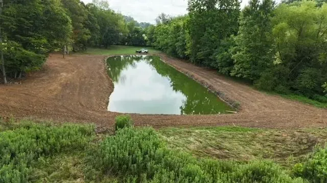 An aerial view of a large pond surrounded by trees and dirt.
