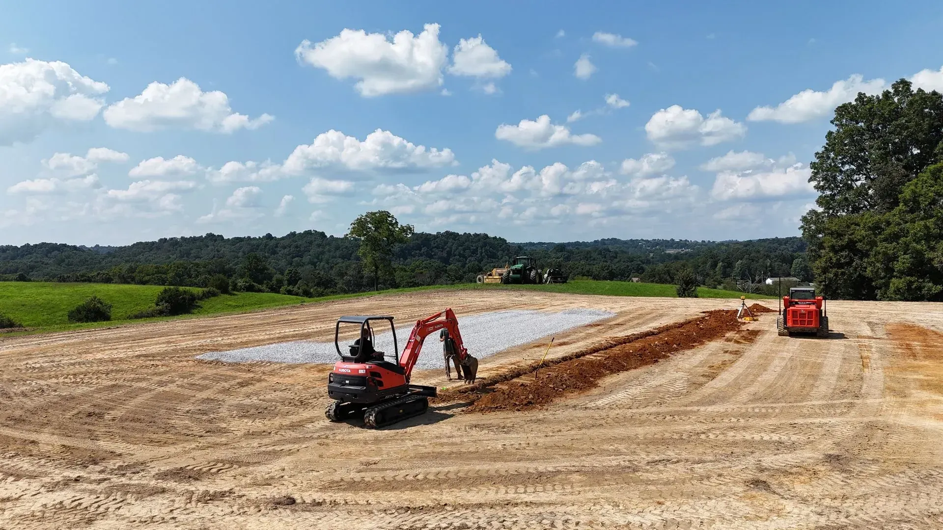 A small red excavator is digging a hole in a dirt field.