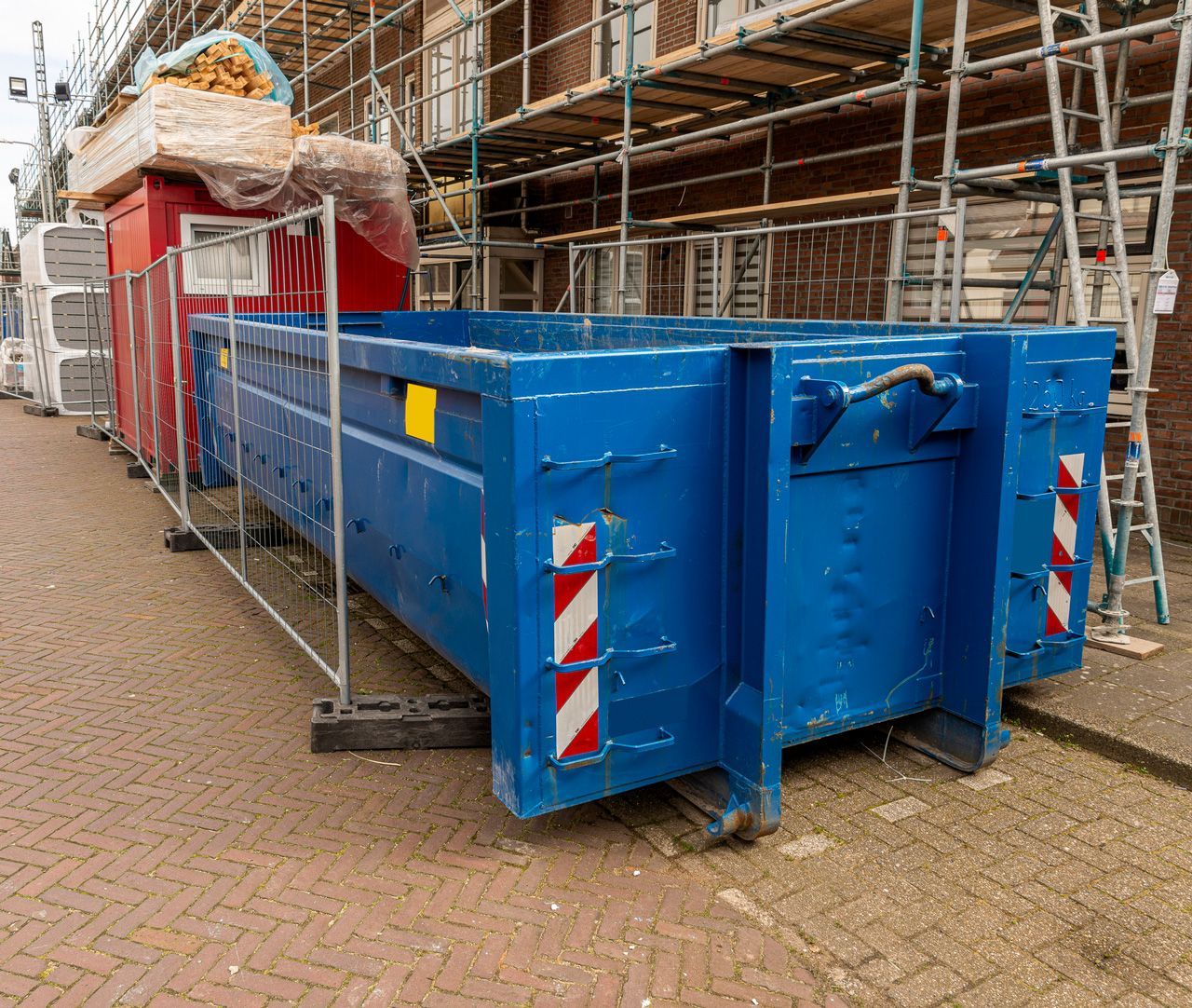 A blue dumpster is parked in front of a building under construction.