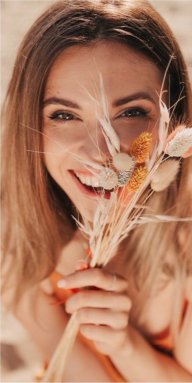 Pretty Lady Covering Face With Summer Flowers — Facial Rejuvenation in Newcastle, NSW