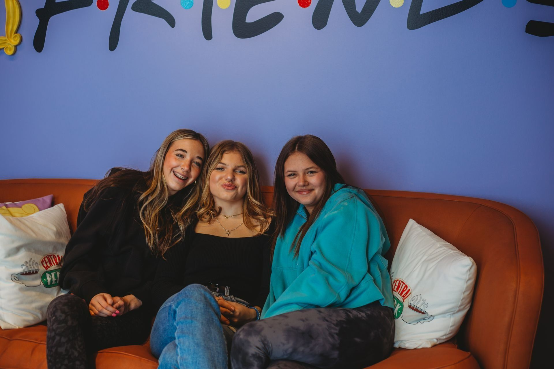 Three people smiling on an orange couch in front of a purple wall with 