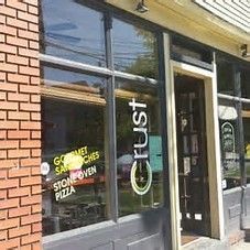 Crust restaurant exterior with glass windows, door, and signage for gourmet sandwiches and stone oven pizza.