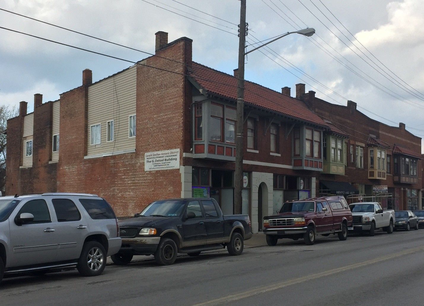 Row of brick buildings with parked cars in front on a city street. Cloudy sky.