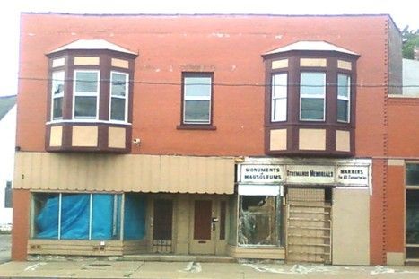 Brick building with two bay windows and a central window above the storefront, partially boarded up.