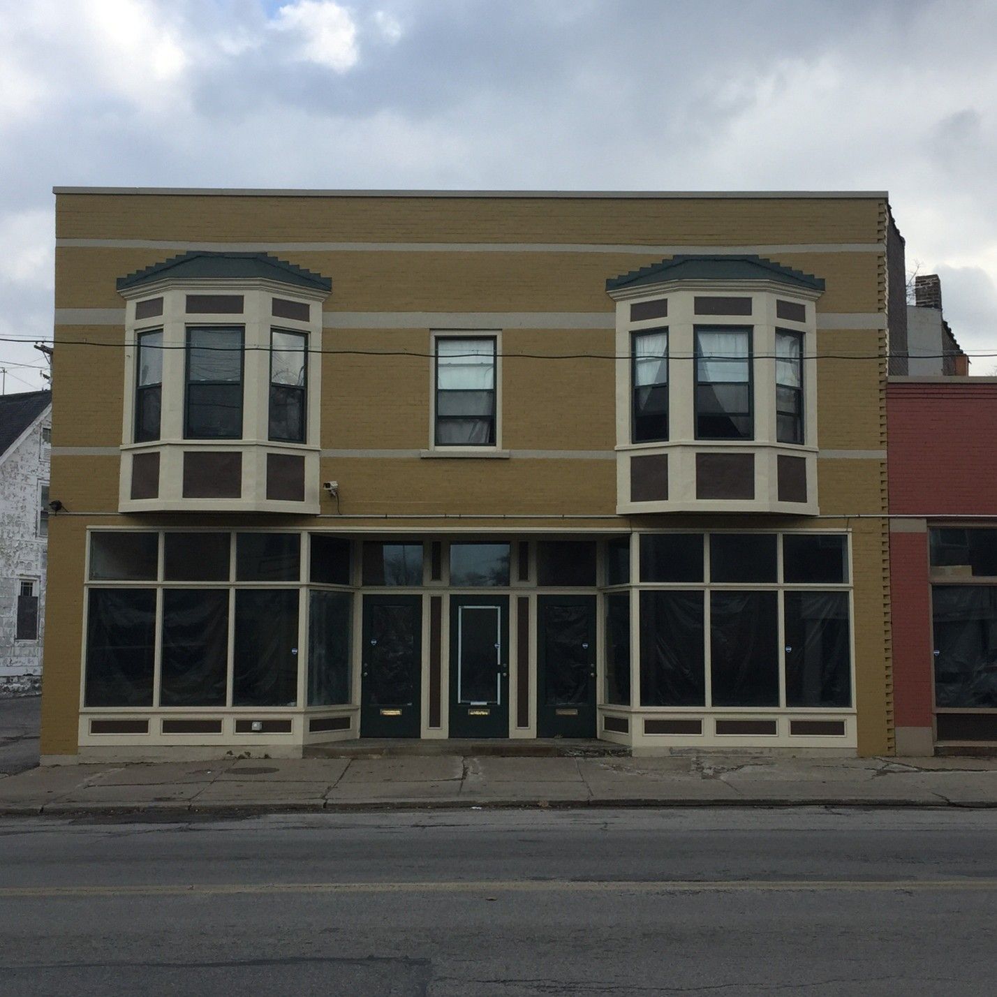 Mustard-colored two-story building with large storefront windows and bay windows on the second floor.