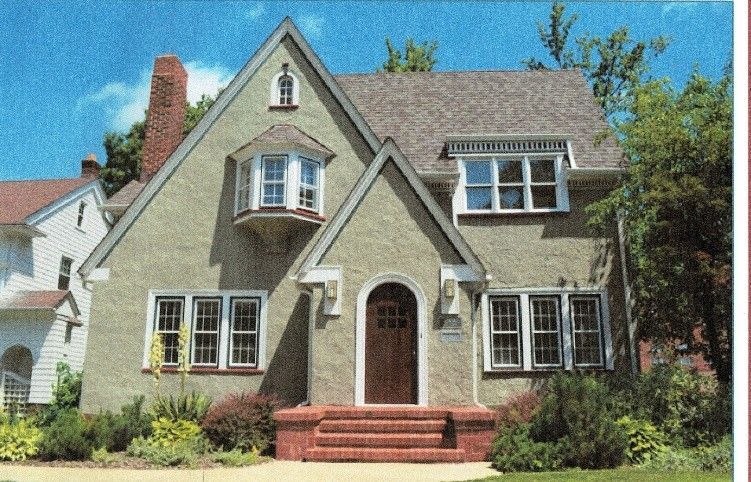 Green stucco house with arched front door, small bay window, and gabled roof.