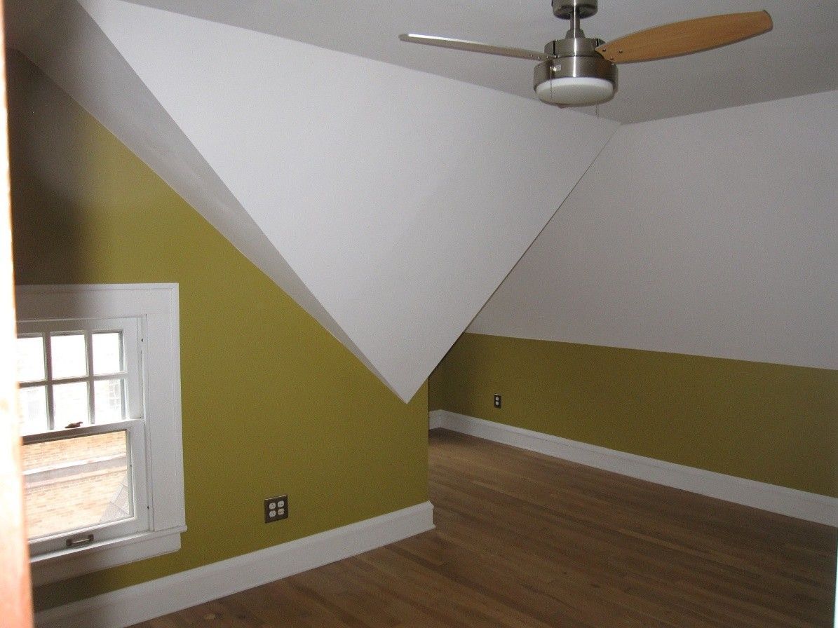 A room with angled walls, wood floor, and green and white paint. A window and ceiling fan are present.