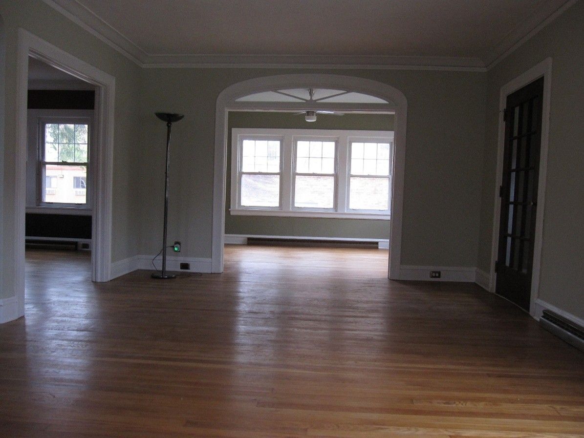 Empty living room with hardwood floors and arched doorway leading to a sunlit area.
