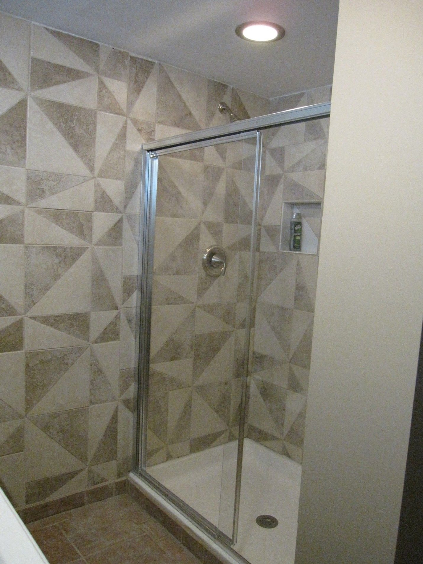 Shower stall with geometric patterned tile walls and a glass door.