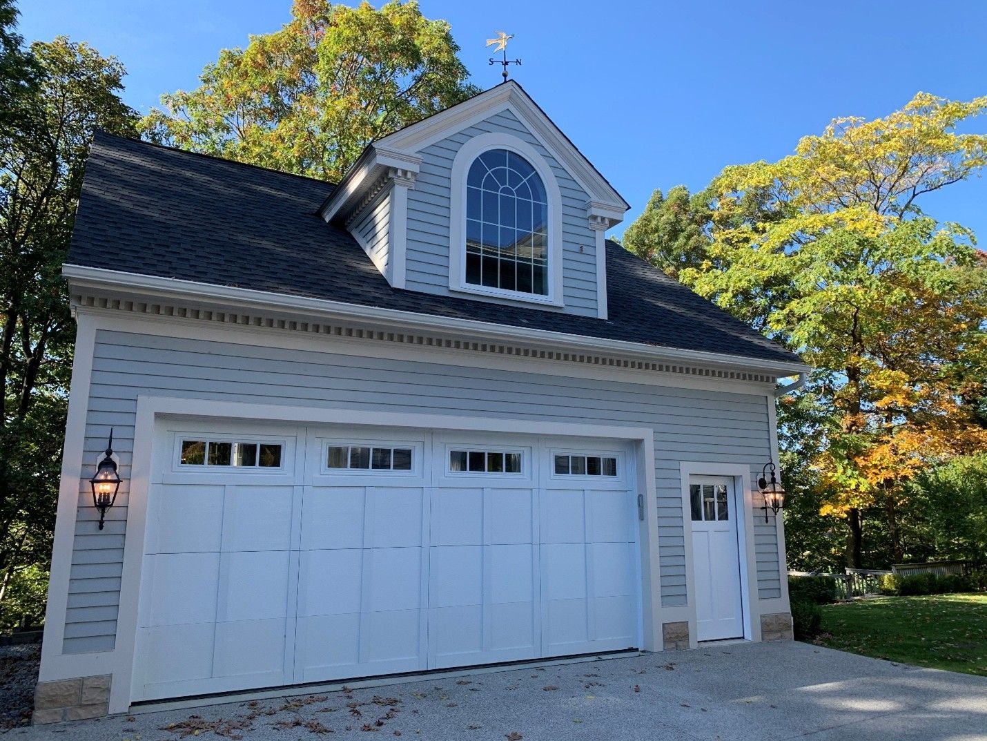 Light blue garage with white doors, dormer window, and black roof.