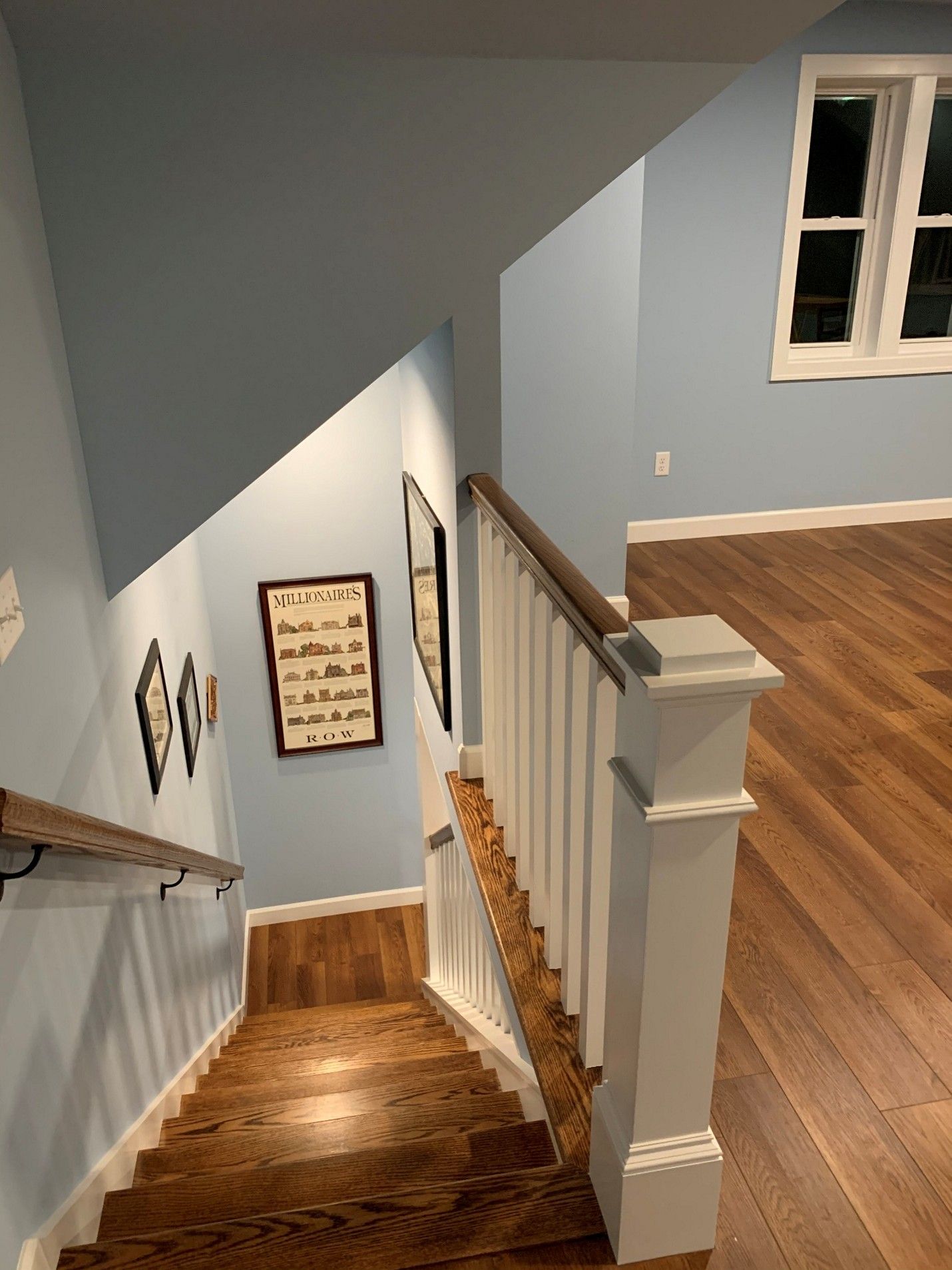 Staircase with wooden steps and handrails. Blue walls, framed art, and a window.