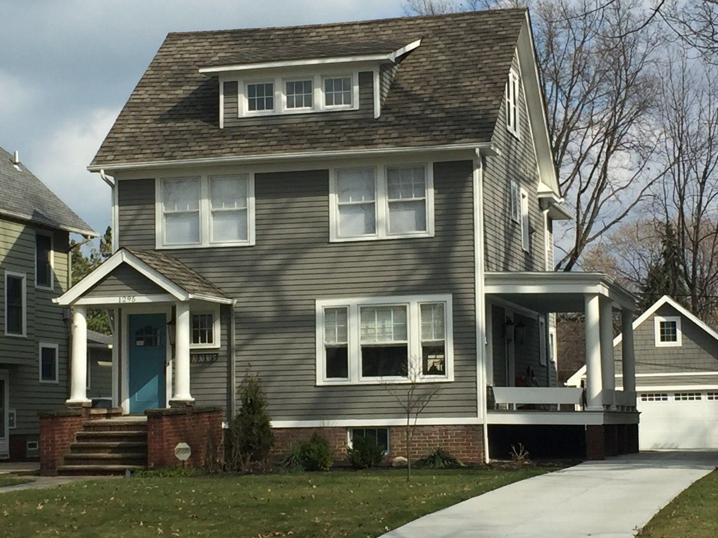 Two-story gray house with white trim, porch, and a dormer. Blue front door. A driveway leads to a garage.