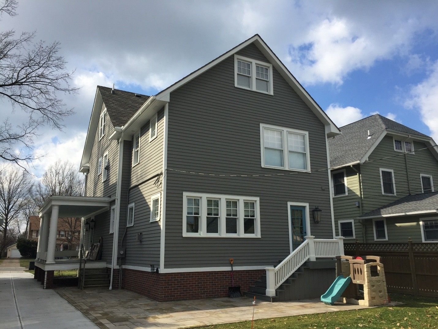 Gray house with white trim, brick foundation, and small porch. Sunny day, lawn with kids' play structure.