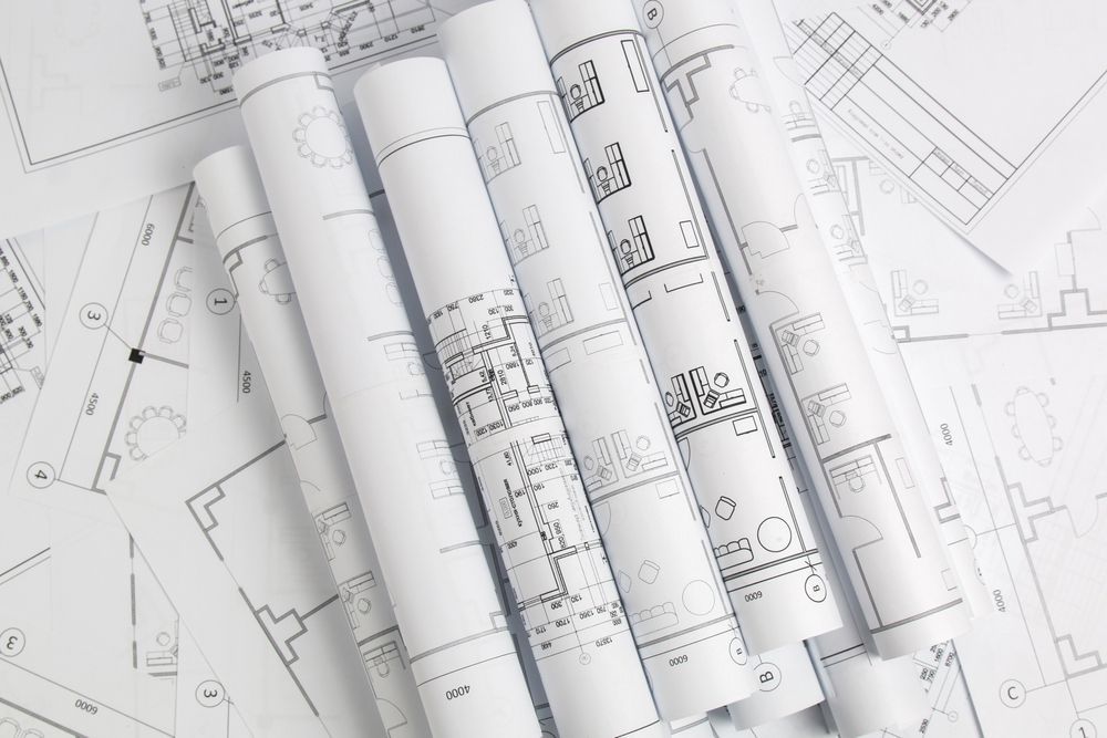 Rolled architectural blueprints, several on top of others, displaying detailed plans.