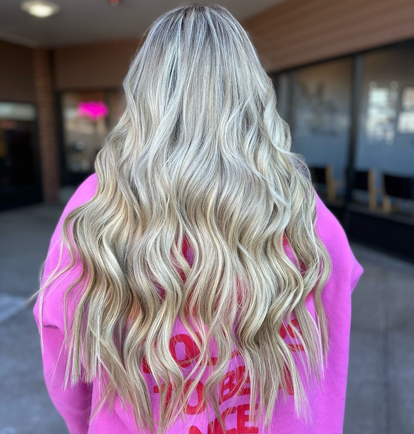 A woman with long blonde hair is wearing a pink sweatshirt.