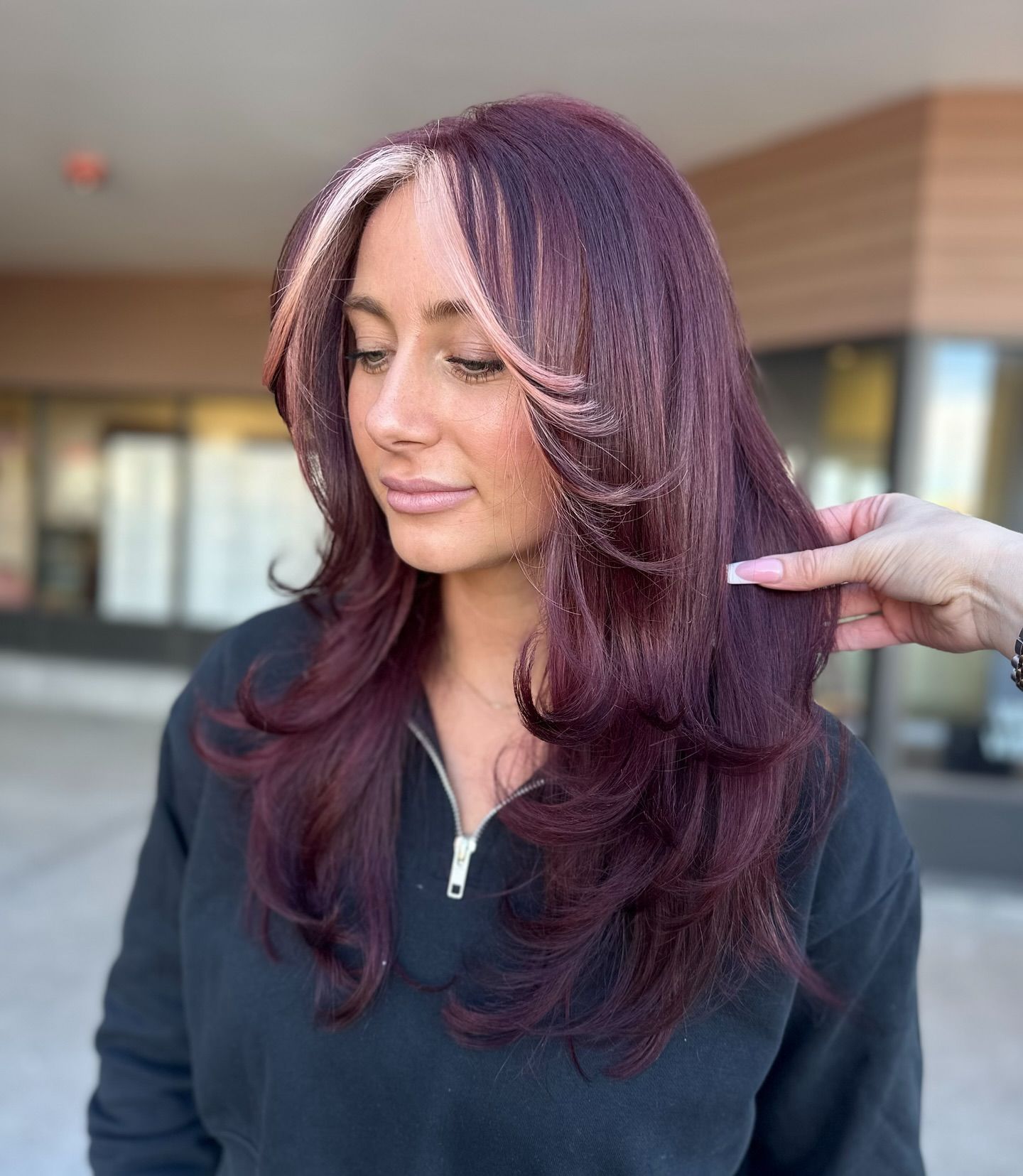 A woman with long purple hair is getting her hair cut by a hairdresser.