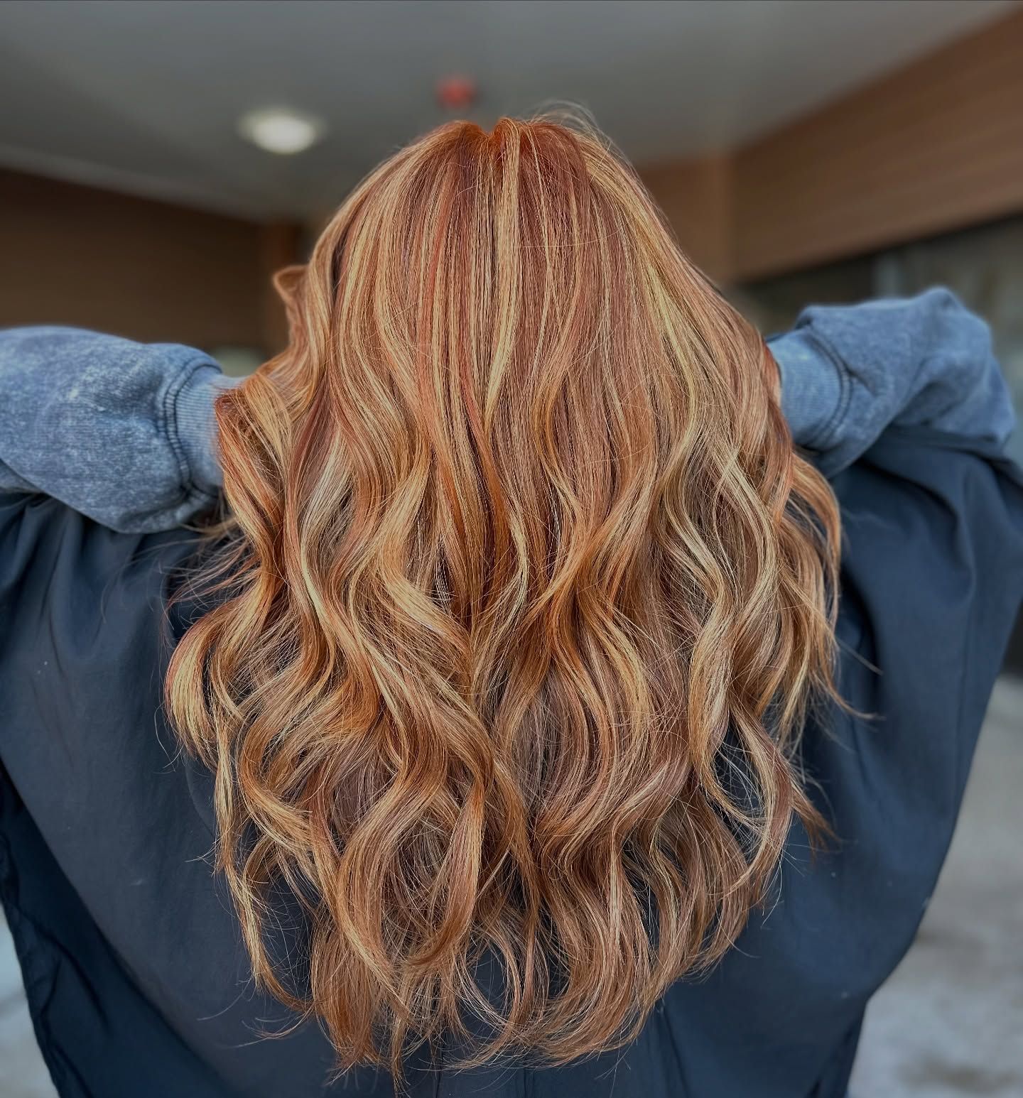 A woman with long red hair is standing with her hands behind her head.