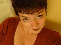 Woman with short dark hair and red shirt looking up at the camera, with dark lipstick and a slight smile.