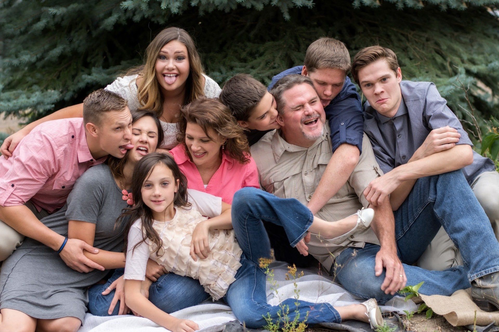 Family of 10 smiling and laughing together outdoors. Various skin tones, with expressions of joy, embracing each other.