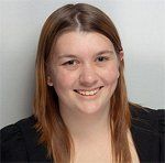 Smiling woman with long, auburn hair and a black top against a gray background.