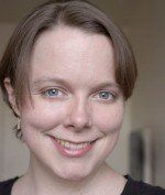 Woman with short brown hair and blue eyes smiling at the camera. Natural light.