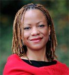 A woman with light brown dreadlocks smiles warmly, wearing a red sweater.