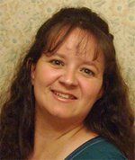 Woman with brown hair smiling, wearing a teal shirt, against a patterned background.