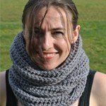 Woman with light skin wearing a thick, gray crocheted cowl outdoors. She smiles at the camera.