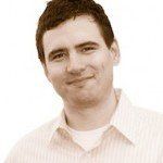 Man smiling, wearing a light-colored button-down shirt and a white undershirt, against a sepia-toned background.