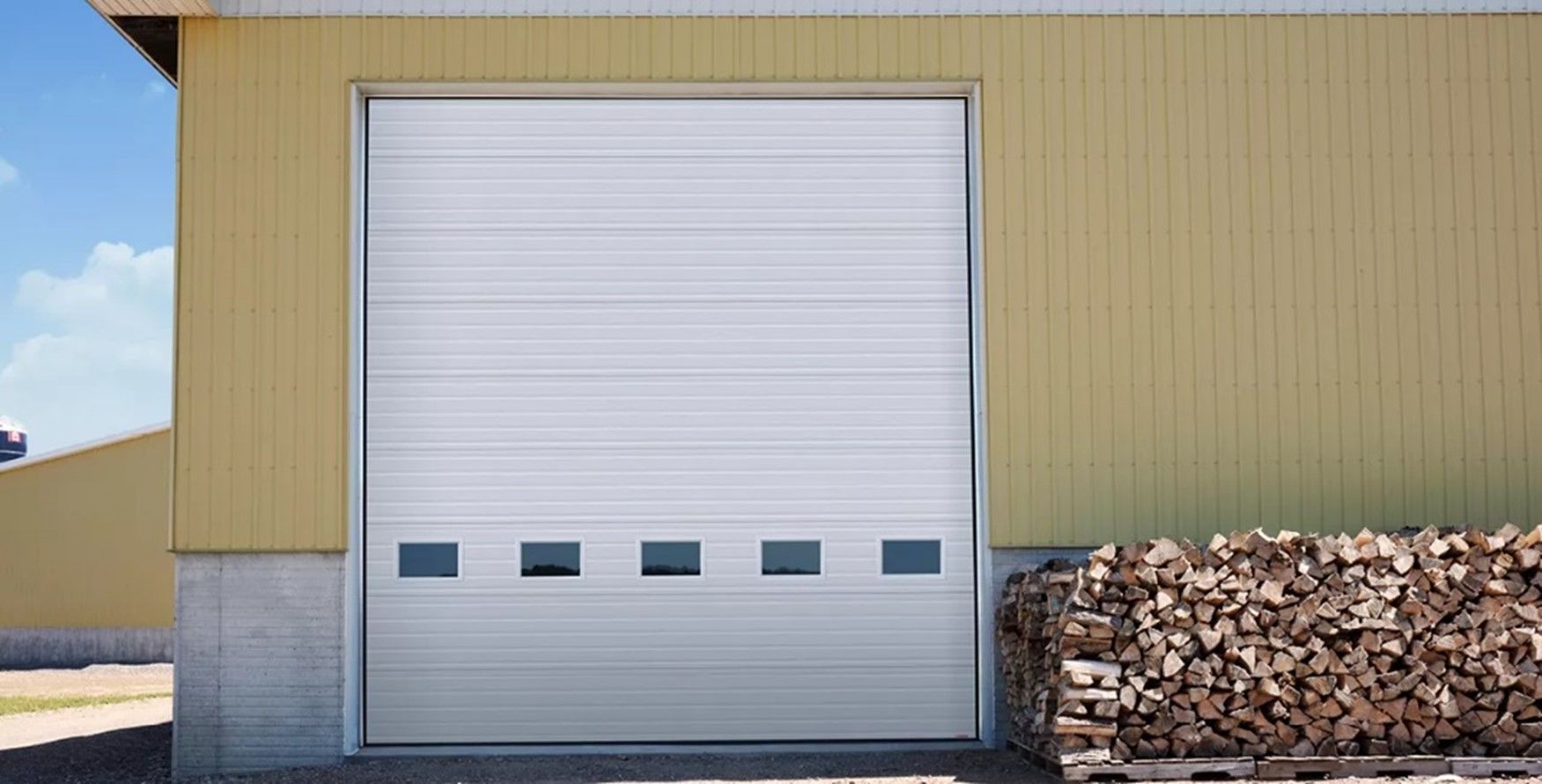 A white garage door is open next to a pile of logs.