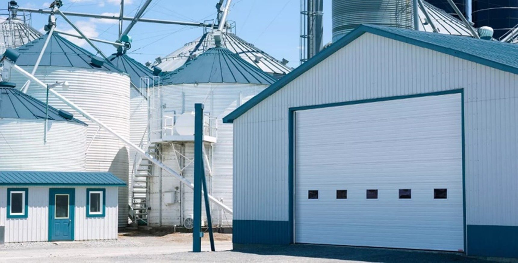 A white building with a blue roof is next to a silo.