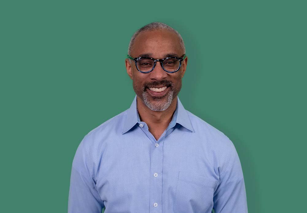 A man wearing glasses and a blue shirt is smiling for the camera.