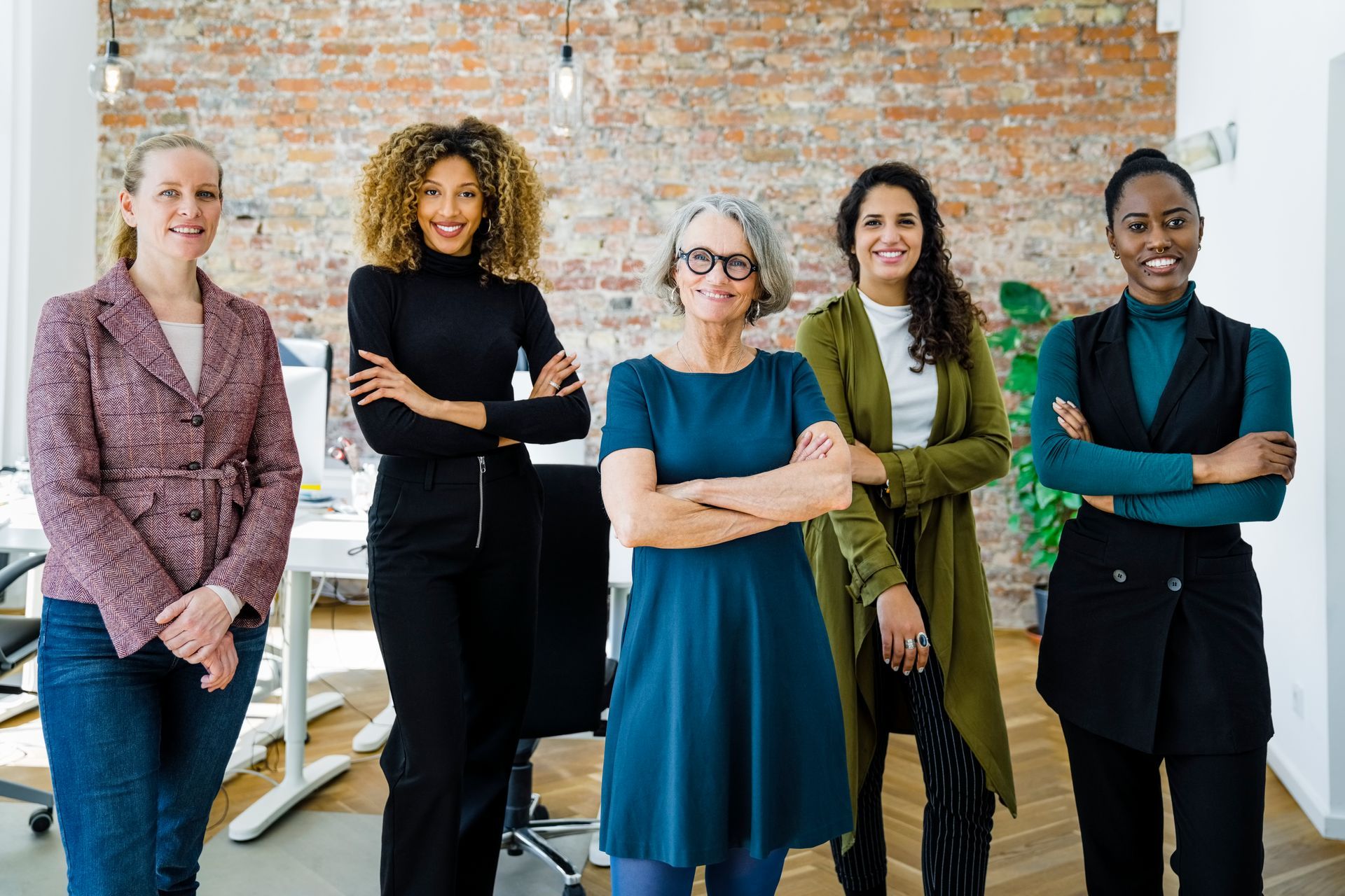A group of women are standing next to each other in an office with their arms crossed.