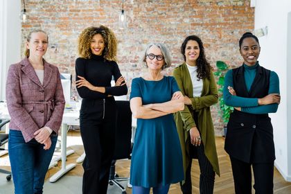 A group of women are standing next to each other in an office with their arms crossed.