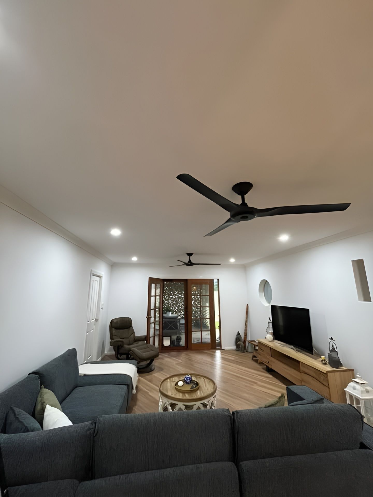 A Living Room With Gray Sectional Sofa, Wooden Floor, and Ceiling Fans — Neave Electrical in Tuncurry, NSW