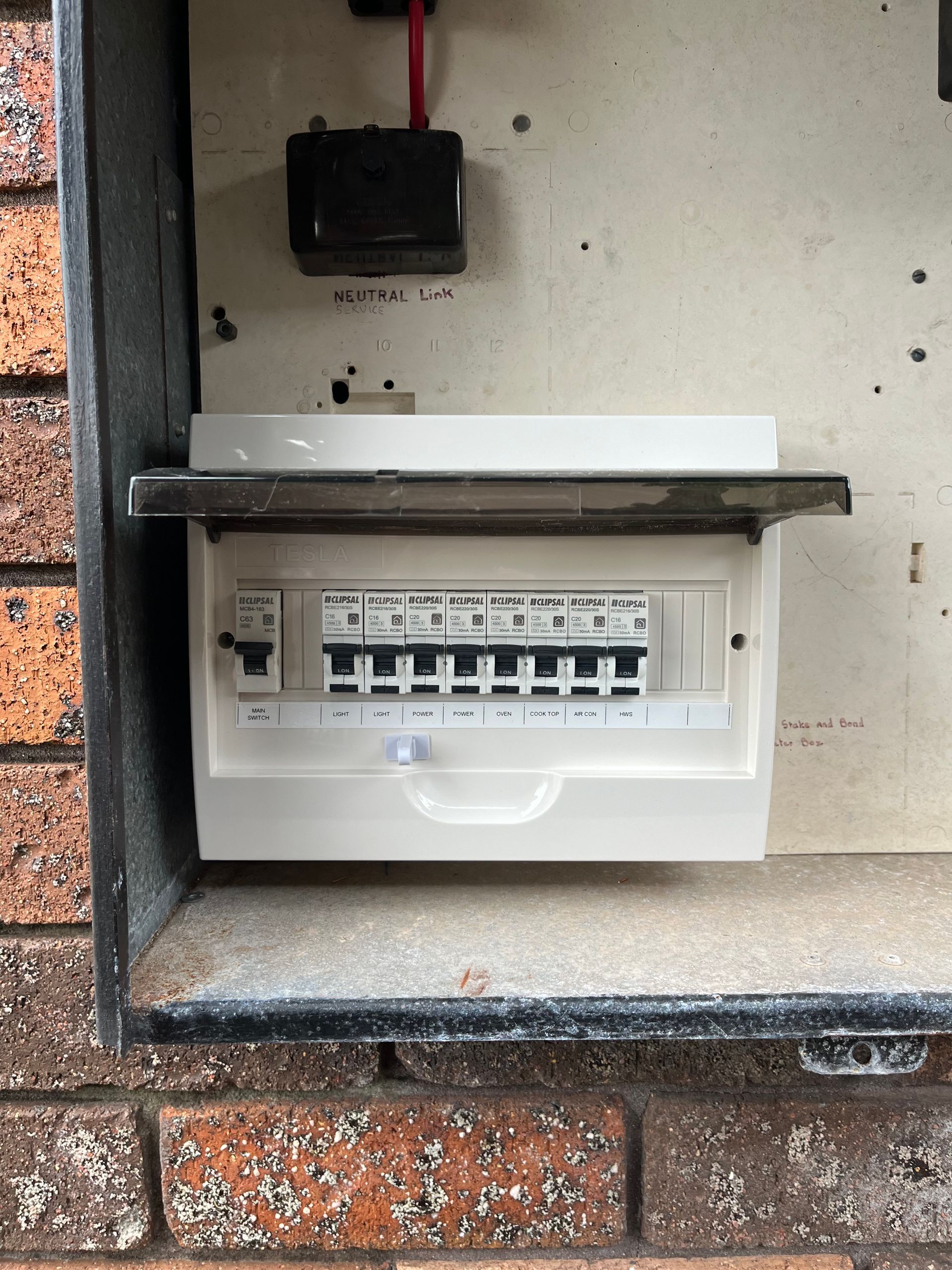 A white electrical panel inside a metal box mounted on a brick wall. The panel door is open. — Neave Electrical in Forster, NSW