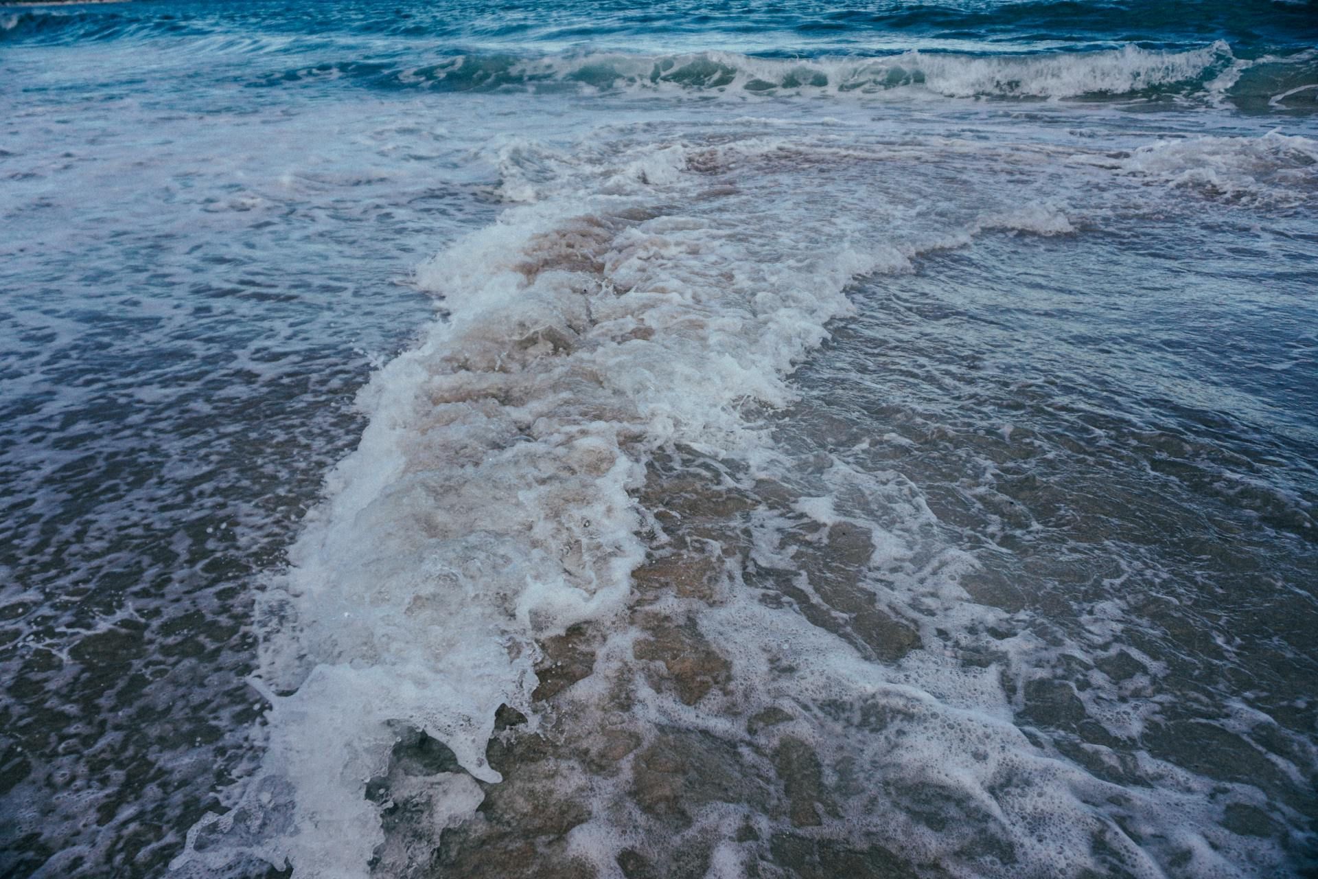 Waves crashing on a sandy shore; foamy white water and blue ocean. — Neave Electrical in Pacific Palms, NSW