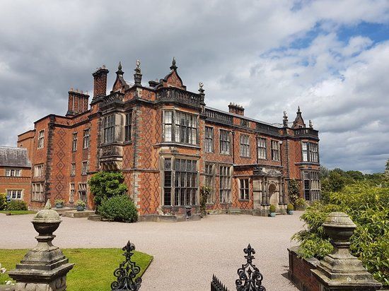 Large brick manor house with ornate details, under cloudy sky.