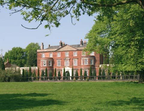 Red brick stately home with green lawn and trees.