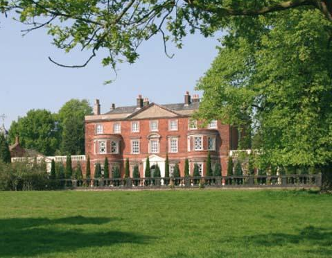 Red brick Georgian mansion with symmetrical facade, set in a grassy landscape.