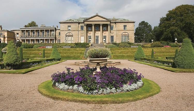 Formal mansion with columns and terraced garden, gravel paths, and flowerbeds.