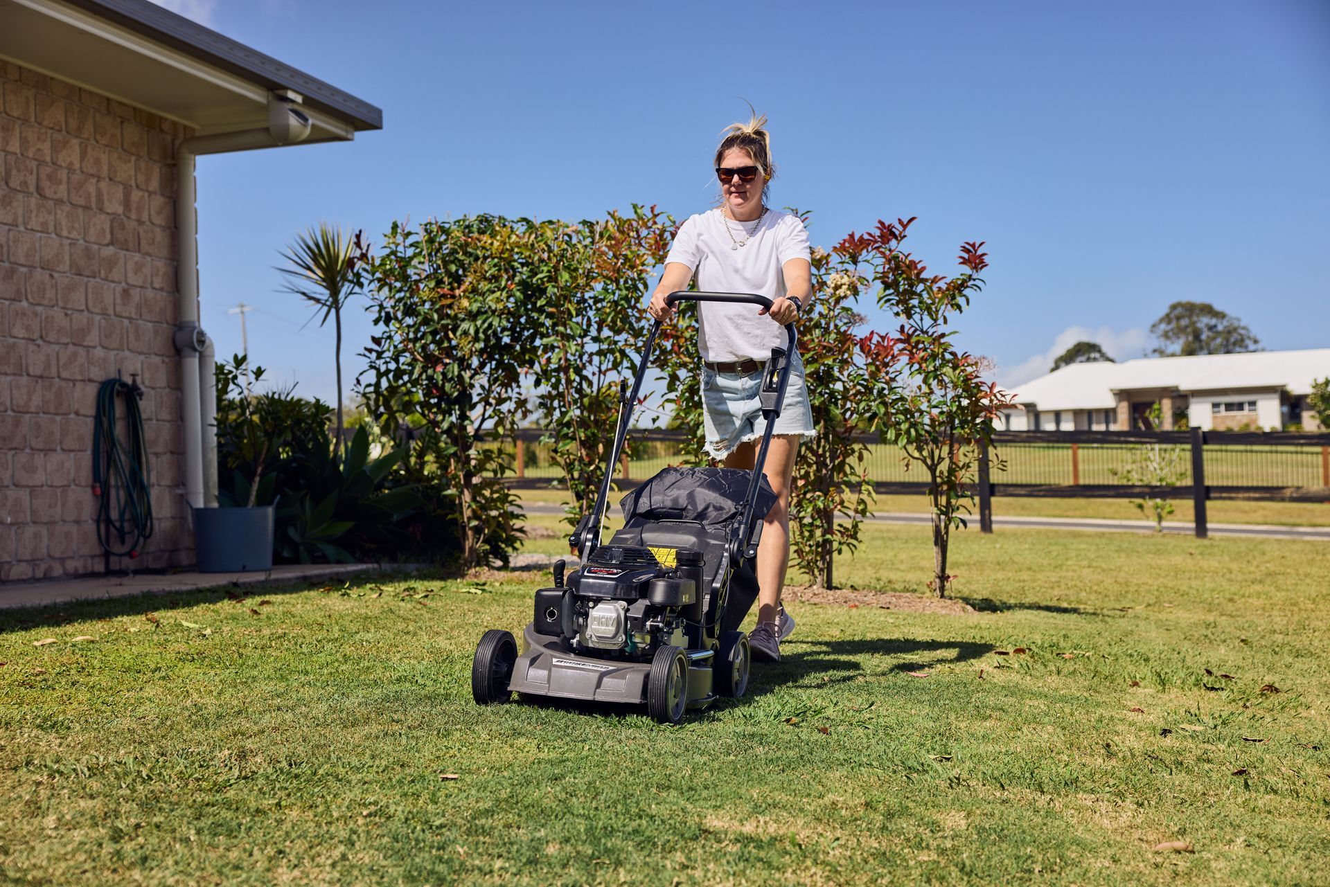 A woman is using a lawn mower to cut the grass in front of a house.