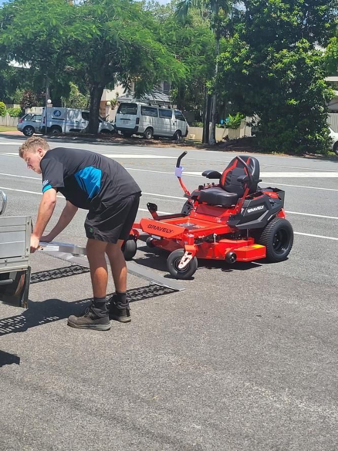 A Man Is Standing Next To A Red Lawn Mower In A Parking Lot — Cairns Mower City In Parramatta Park, QLD