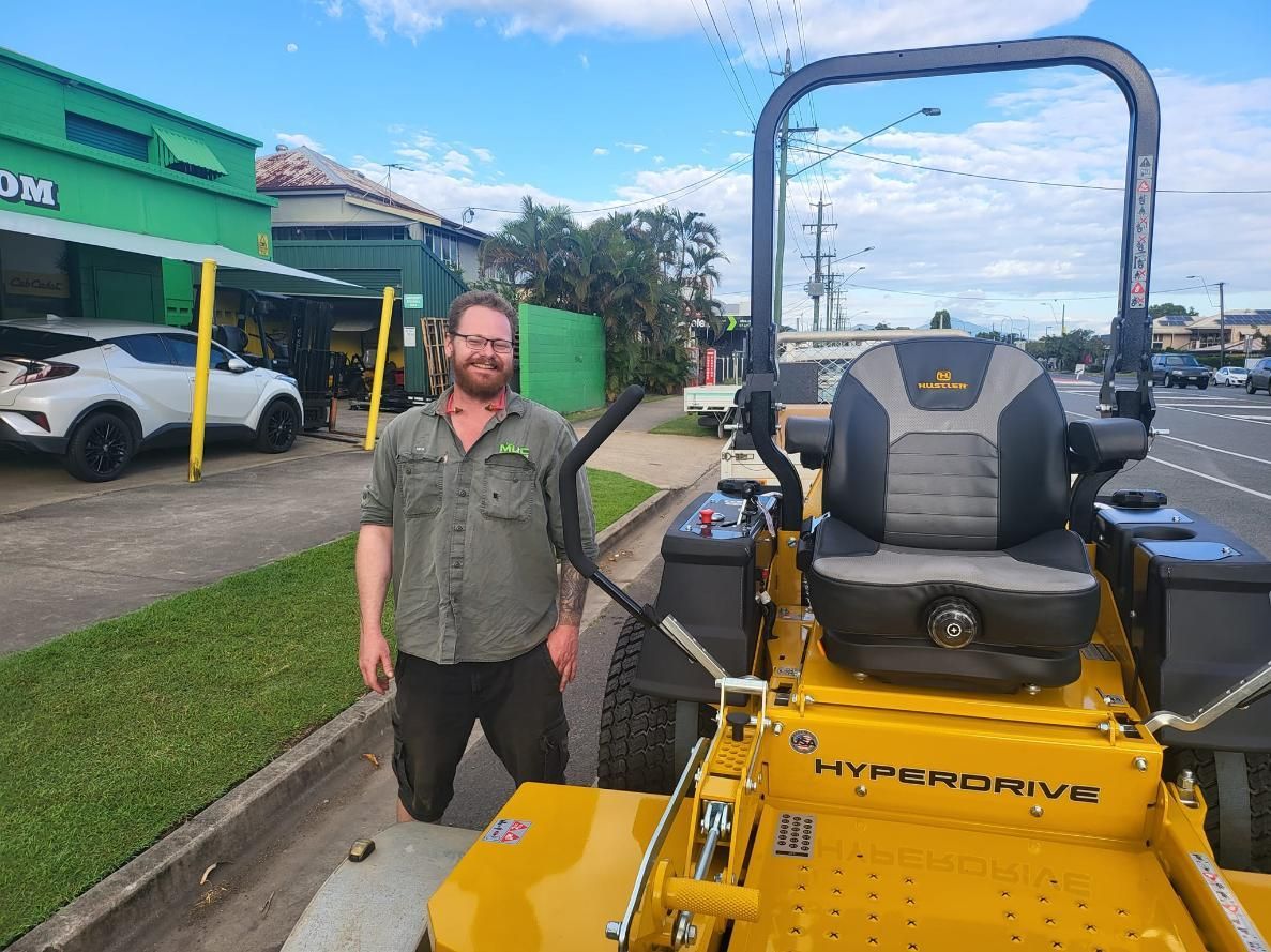 A Man Is Kneeling Next To A Yellow Lawn Mower — Cairns Mower City In Parramatta Park, QLD