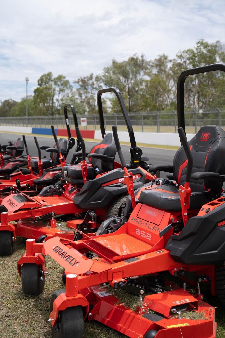 A Row Of Red Lawn Mowers Are Parked On The Grass — Cairns Mower City In Parramatta Park, QLD