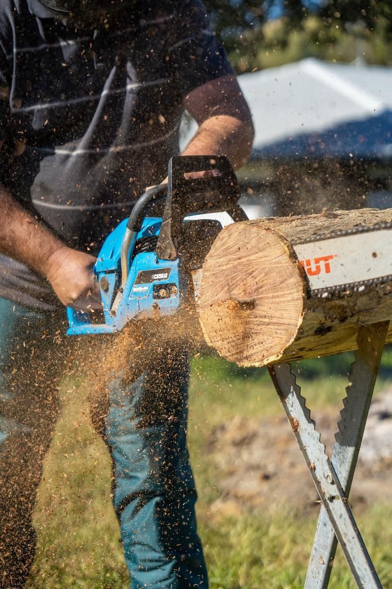 A Man Is Cutting A Log With A Chainsaw — Cairns Mower City In Parramatta Park, QLD