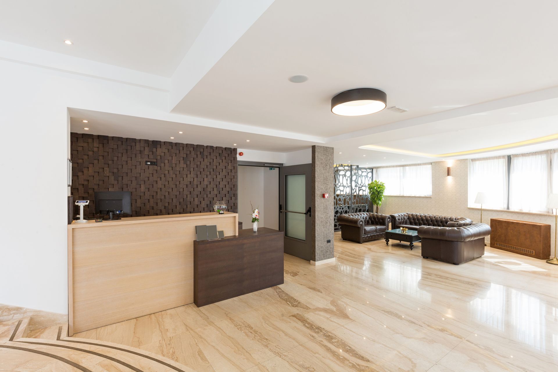 Modern open-plan living room with beige floor, dark sofa, reception desk, and large windows