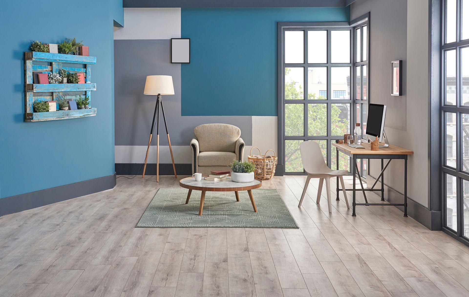 Modern living room with blue walls, gray chair, floor lamp, coffee table, desk, and window seating area.