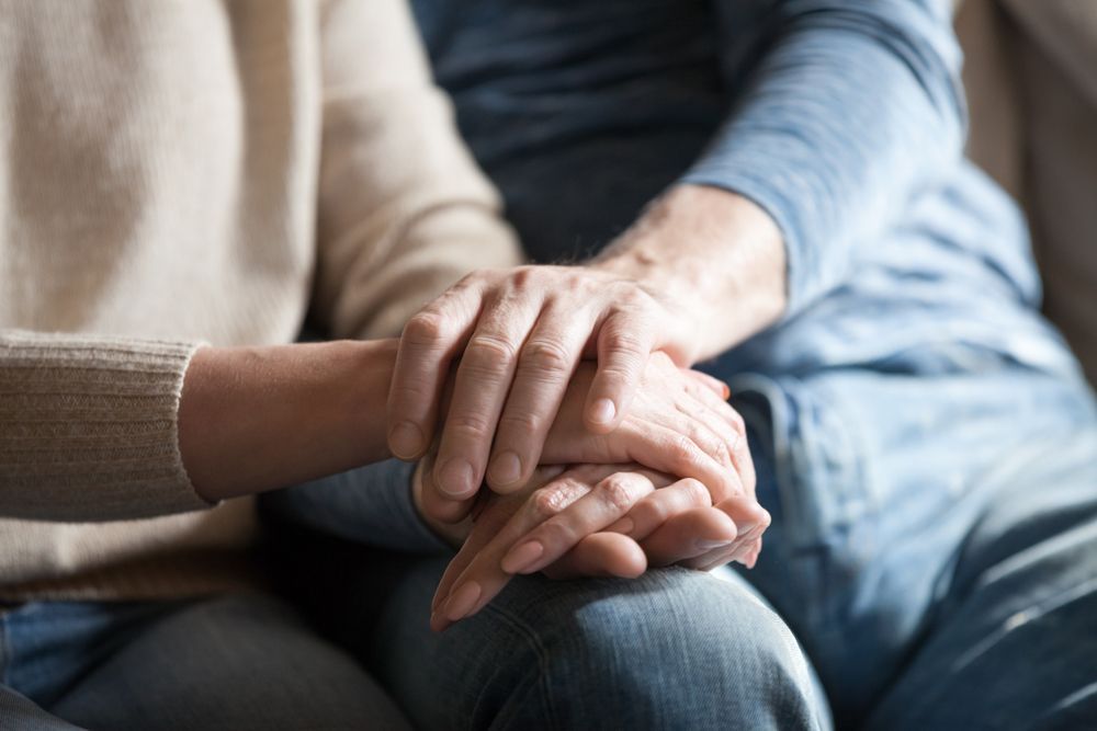 Two people sitting together, holding hands in a comforting gesture — Ashes to Ashes Cremations In Mooroobool, QLD