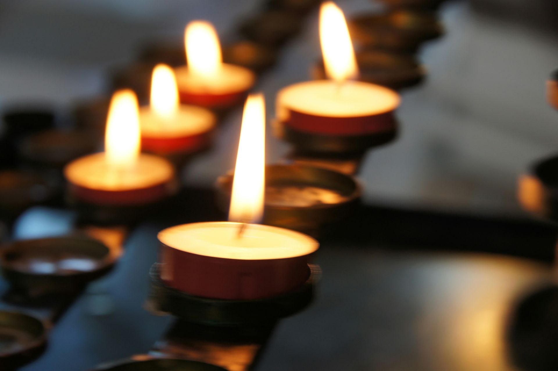 Lit tealight candles arranged in rows, with warm flames glowing in a dark setting — Ashes to Ashes Cremations In Mooroobool, QLD